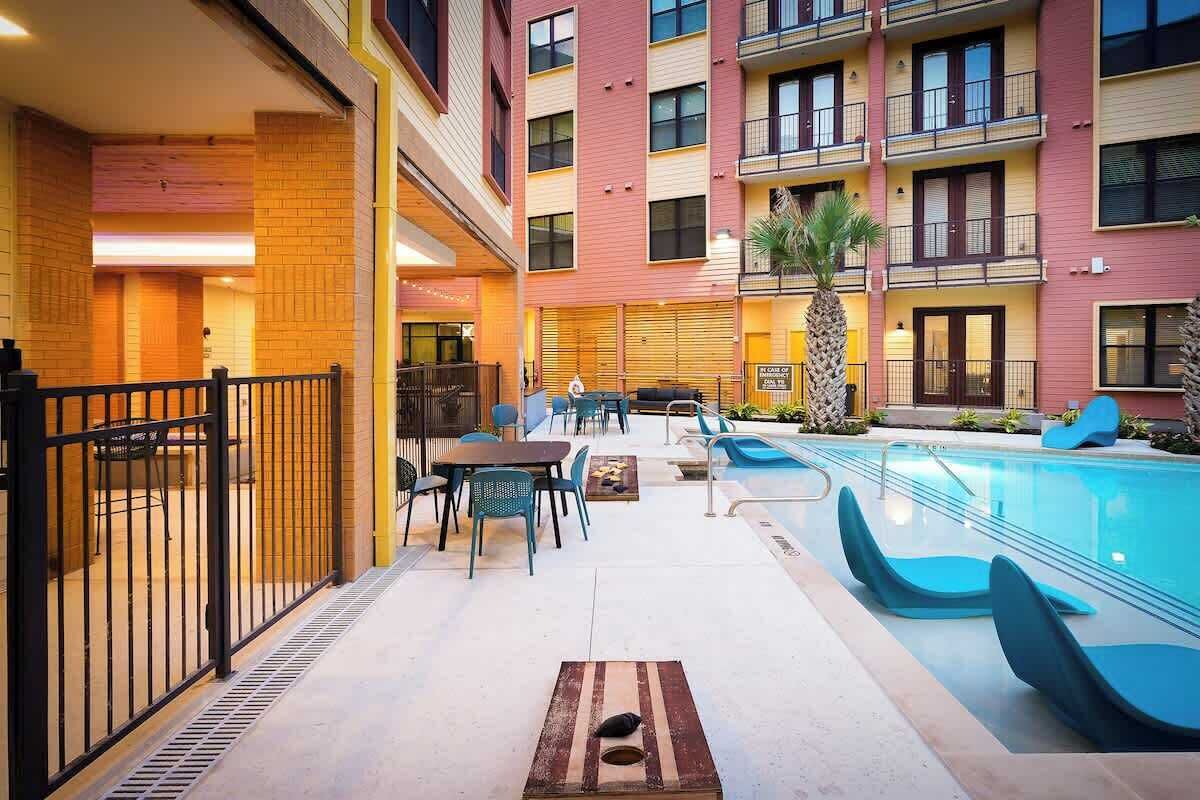 An indoor pool area with a pool, lounge chairs, and tables.