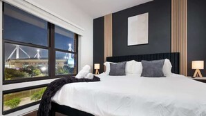 Una habitación de hotel moderna con una cama grande, vista de un puente de noche y una pared oscura con líneas verticales.