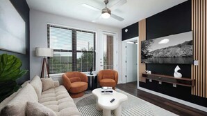 A modern living room with a sofa, two armchairs, a coffee table, a TV, and a ceiling fan.