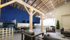 An outdoor patio area with wooden furniture, including sofas and chairs, under a pergola with string lights. - Snug 1-Bedroom with Gym,  Near Riverwalk & Dome (San Antonio)