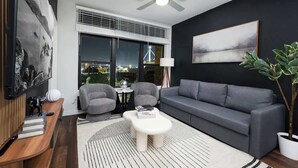 A modern living room with a grey sofa, two armchairs, a white coffee table, and a large window with a view of a bridge. - Snug 1-Bedroom with Gym,  Near Riverwalk & Dome (San Antonio)