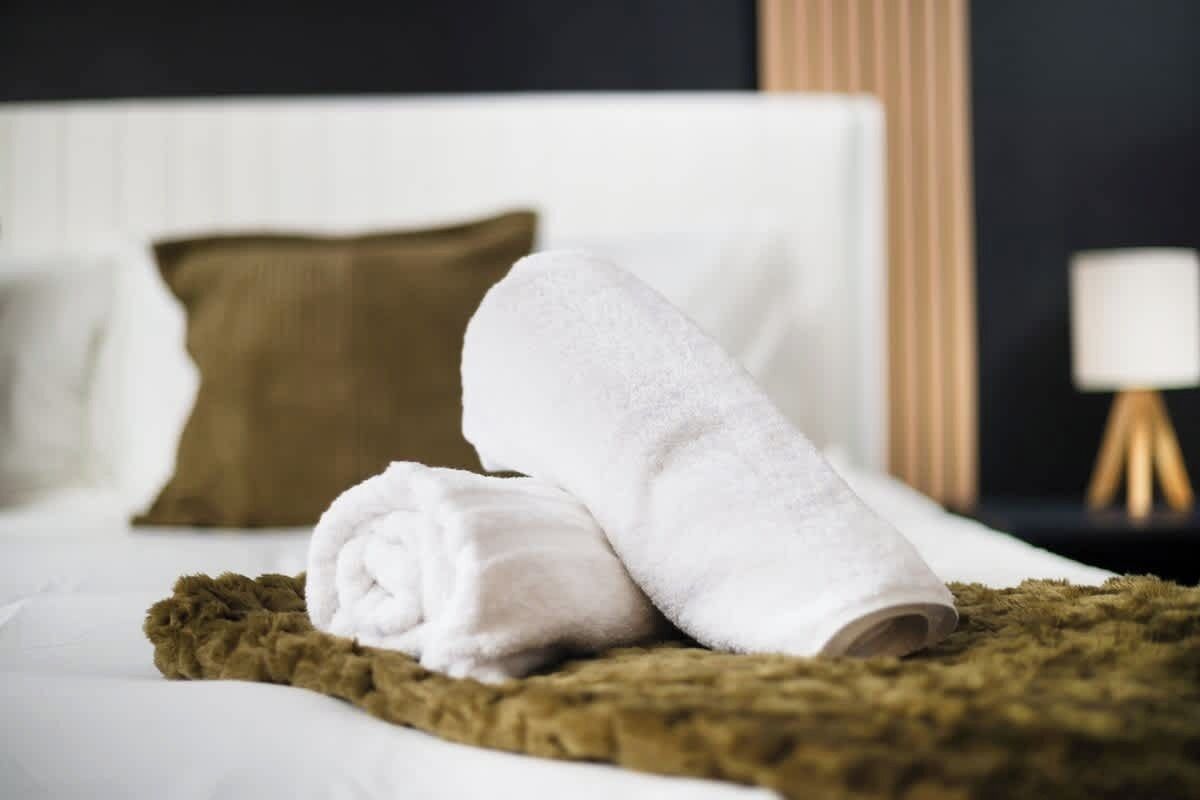 A neatly made bed with white linens and a brown throw blanket.
