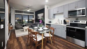 A modern kitchen with grey cabinets, stainless steel appliances, and a dining area with a glass table and wooden chairs. - Snug 1-Bedroom with Gym,  Near Riverwalk & Dome (San Antonio)