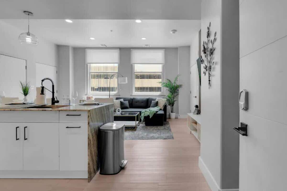 Cocina moderna con armarios blancos, una isla central y un comedor con sofá negro y una mesa pequeña.