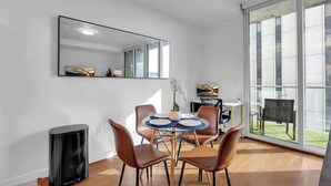 Un comedor moderno con una mesa redonda, sillas marrones, un cesto de basura negro y un ventanal con vistas a un área verde.