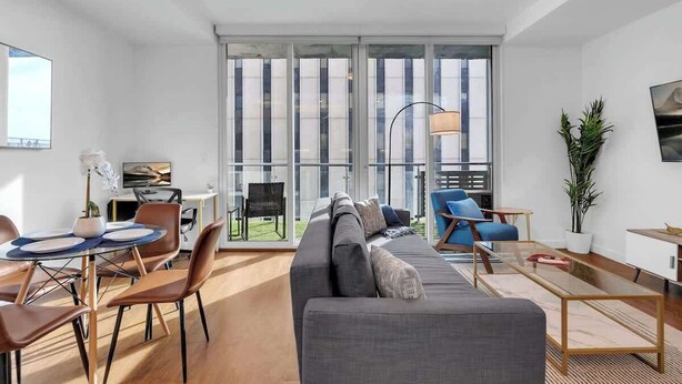 Una sala de estar moderna con un sofá gris, un sillón azul y una mesa de comedor con sillas.