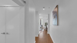 A hallway with white walls and wooden flooring, leading to a dining area with a table and chairs.