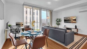 A modern living room with a dining area, a grey sofa, and a flat-screen TV on the wall.