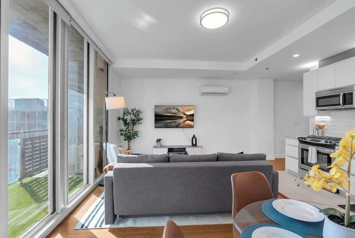 En moderne lejlighed med en stor skydedør, en grå sofa, et spiseområde med bord og stole samt et køkken med komfur og mikroovn.