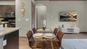 Una cocina moderna con microondas, estufa y comedor con mesa de vidrio y sillas marrones.