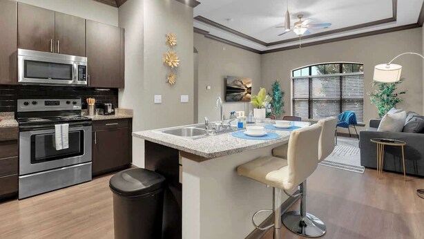 Una cocina moderna con electrodomésticos de acero inoxidable, una isla central con taburetes de bar y un comedor con vistas al exterior.