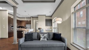 A modern living room with a grey sofa, a coffee table, and a large window with blinds.