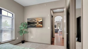 A bedroom with a bed, a potted plant, a painting, and a view of the hallway.