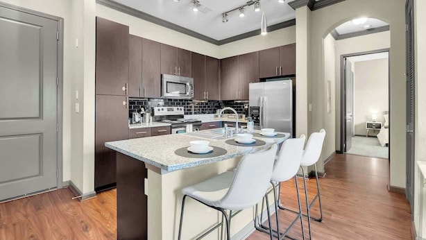 A modern kitchen with dark cabinets, stainless steel appliances, and a central island with bar stools.
