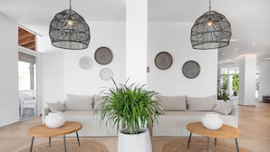 Una sala moderna con un sofá, dos mesitas auxiliares, una planta grande en maceta y platos decorativos en la pared.