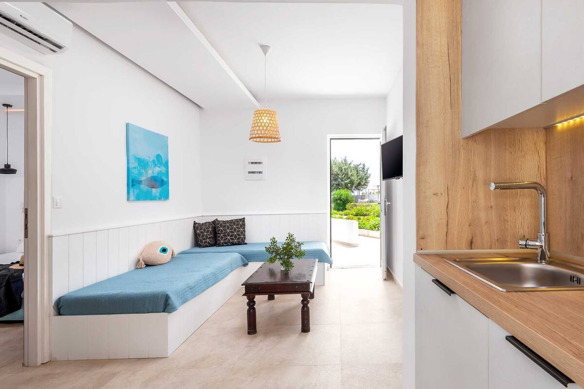 Een moderne keuken met een houten aanrecht en een spoelbak, een blauwe bank met kussens, een kleine tafel met een plant en een schilderij aan de muur.