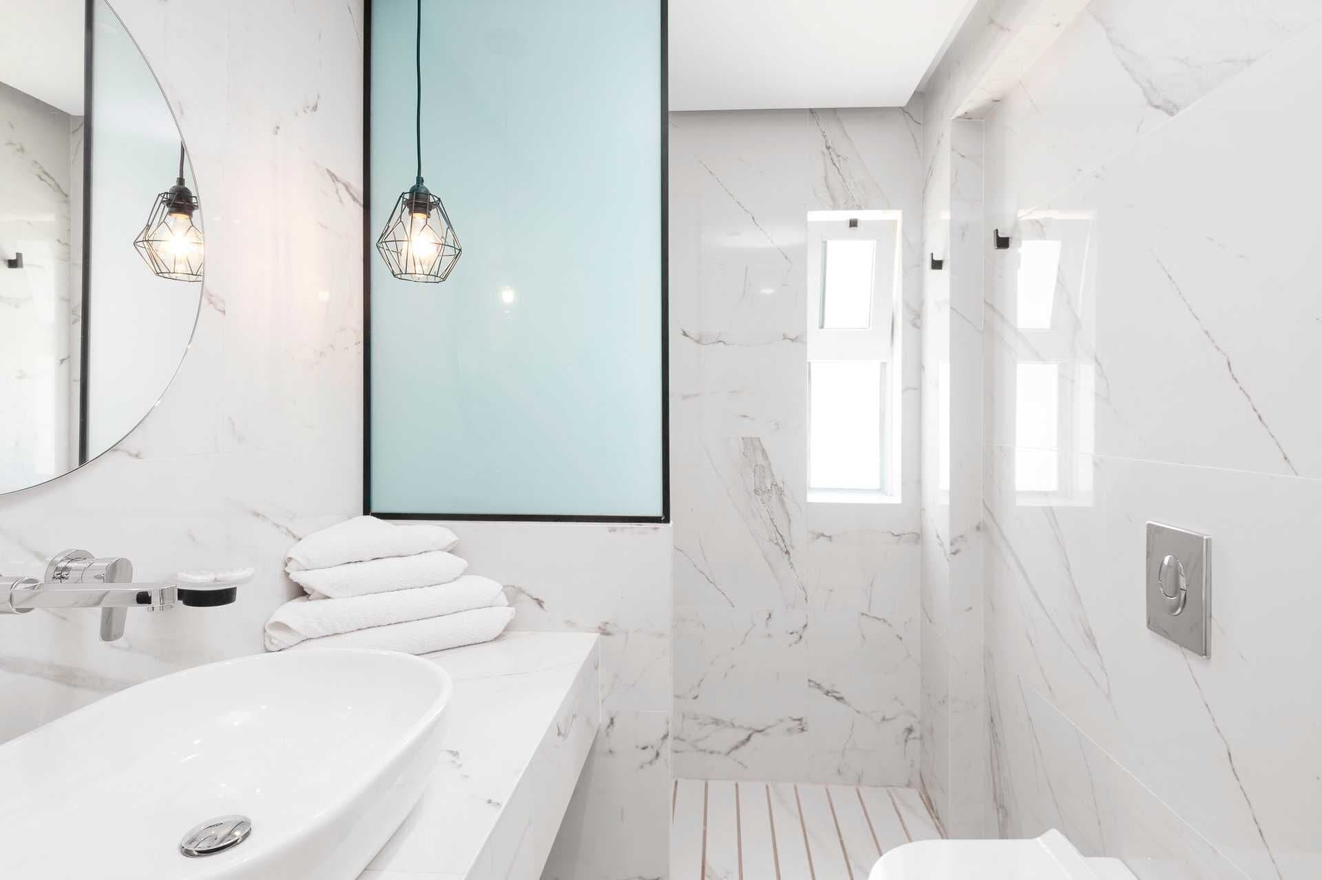 A modern bathroom with a large mirror, two pendant lights, a white sink, and a shower area.