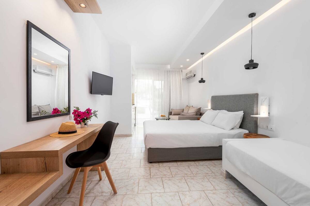 Een moderne hotelkamer met een bureau, twee bedden, een televisie en een grote spiegel.