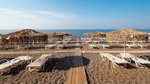 Una playa con pasarelas de madera, sombrillas de paja y tumbonas blancas.