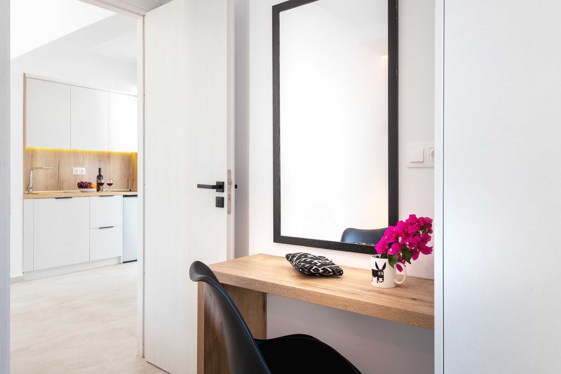 A modern room with a wooden desk, a large mirror, and a view into a kitchen area.