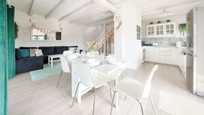 A modern kitchen with white cabinets, a dining area with a white table and chairs, and a staircase leading to an upper level. - Dom Marcello Sun & Snow  (gmina Wolin)