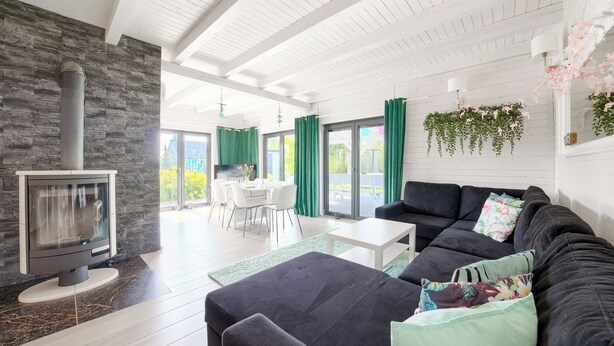 A modern living room with a fireplace, a sofa, a dining area, and large windows. - Dom Marcello Sun & Snow  (gmina Wolin)