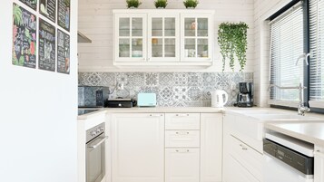 Una cocina con armarios blancos, microondas, tostadora, cafetera y una planta colgante.