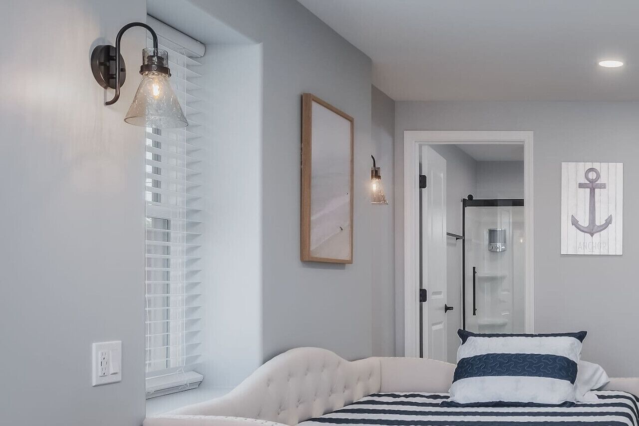 Een slaapkamer met een bed, een wandlamp, een lijst met een afbeelding en een deur naar een badkamer.