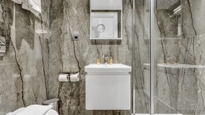 Un bagno moderno con rivestimento in marmo, un lavabo bianco con due rubinetti, un water e un box doccia in vetro.