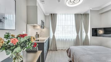 Una habitació d'hotel moderna amb un llit, una taula de treball amb un vas de flors, un televisió de pantalla plana i una finestra gran amb cortines.
