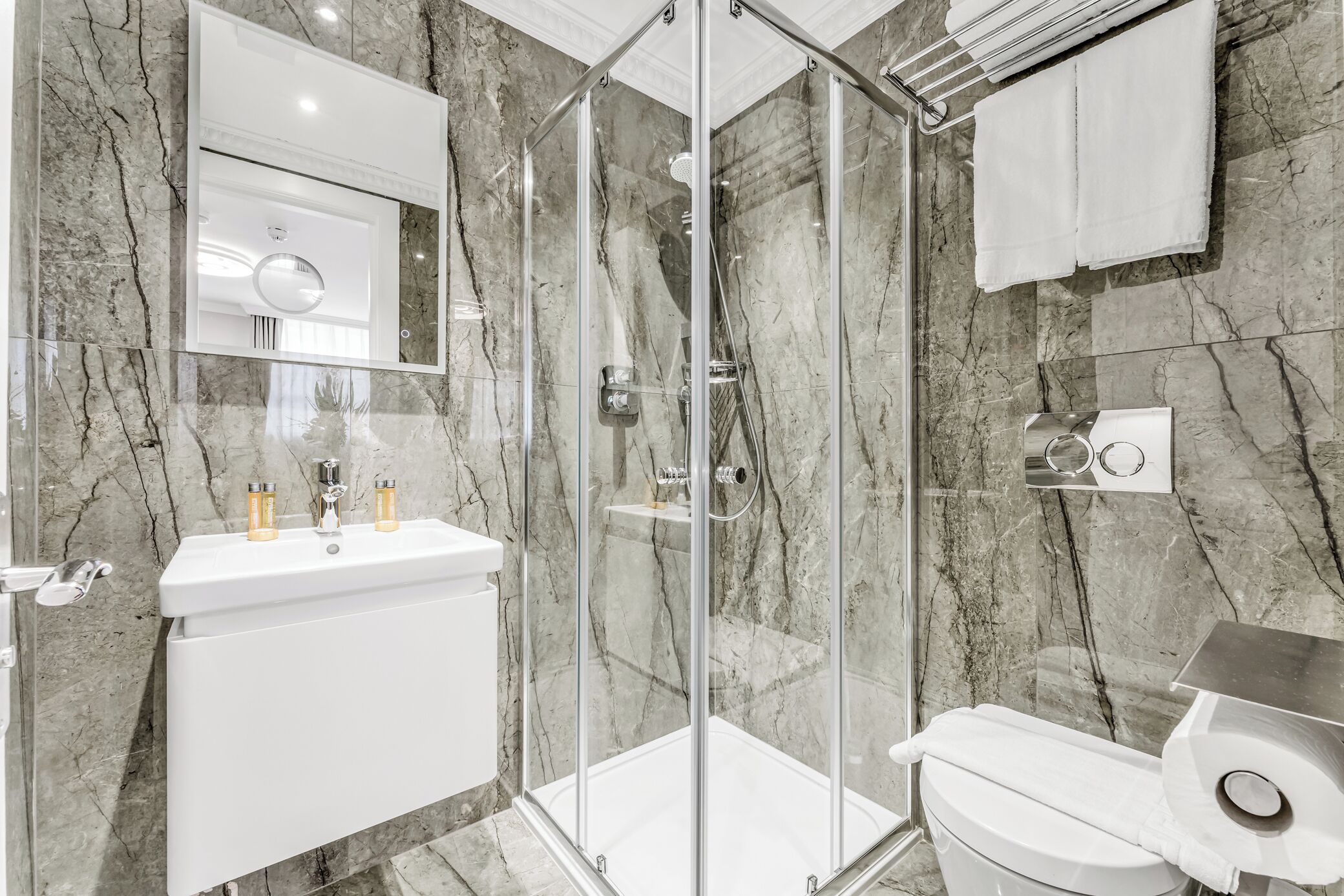 A modern bathroom with a glass-enclosed shower, a white sink with two faucets, and a toilet.