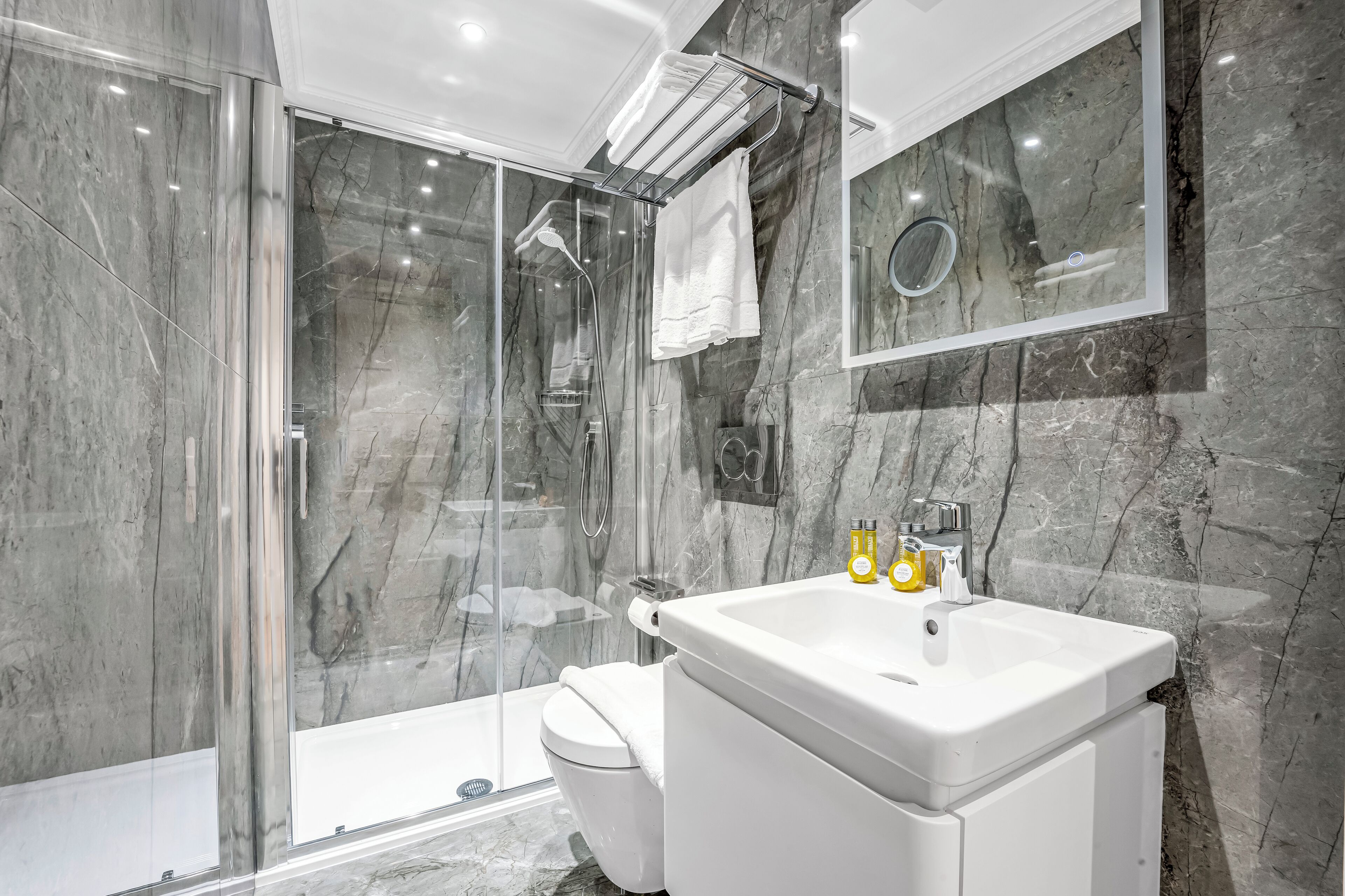 Un bany modern amb dutxa d'estuc de vidre, un lavabo blanc i una paret de marbre.