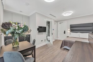 Una sala de estar moderna con un sofá, una mesa de comedor con sillas, un televisor montado en la pared y un jarrón con flores sobre la mesa.