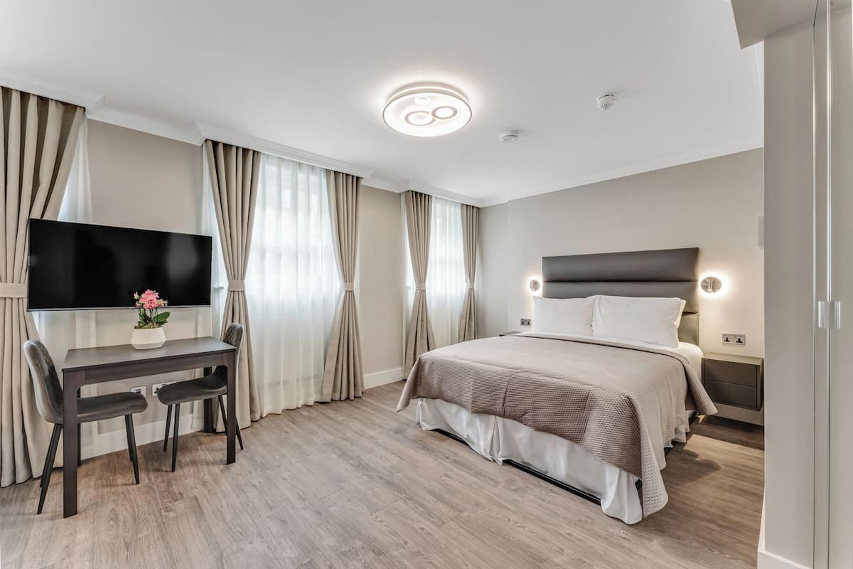 Una moderna camera d'albergo con un letto grande, una scrivania con sedia, una TV a schermo piatto e una lampada a soffitto.