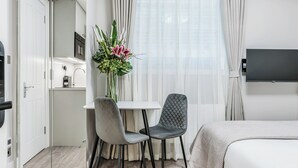Una moderna camera d'albergo con un letto, una scrivania con due sedie, una TV e una finestra con tende.