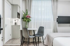 Una habitación de hotel moderna con una cama, un escritorio con dos sillas, un televisor y una ventana con cortinas.