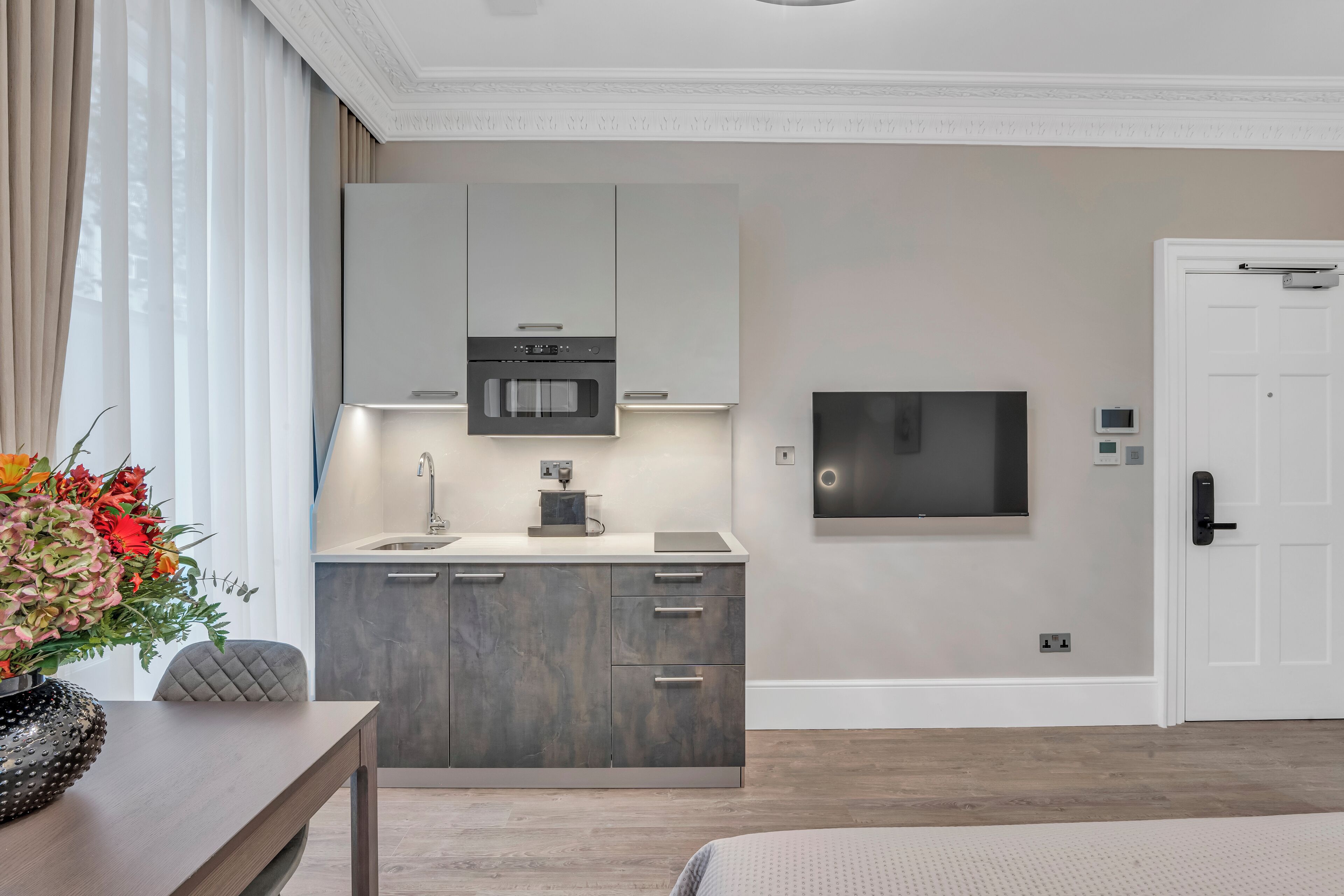 A modern kitchen with a built-in oven, a coffee machine, and a flat-screen TV mounted on the wall.