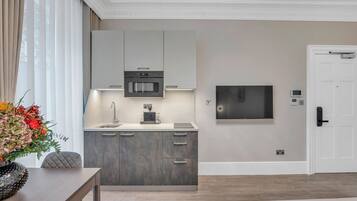 A modern kitchen with a built-in oven, a coffee machine, and a flat-screen TV mounted on the wall.
