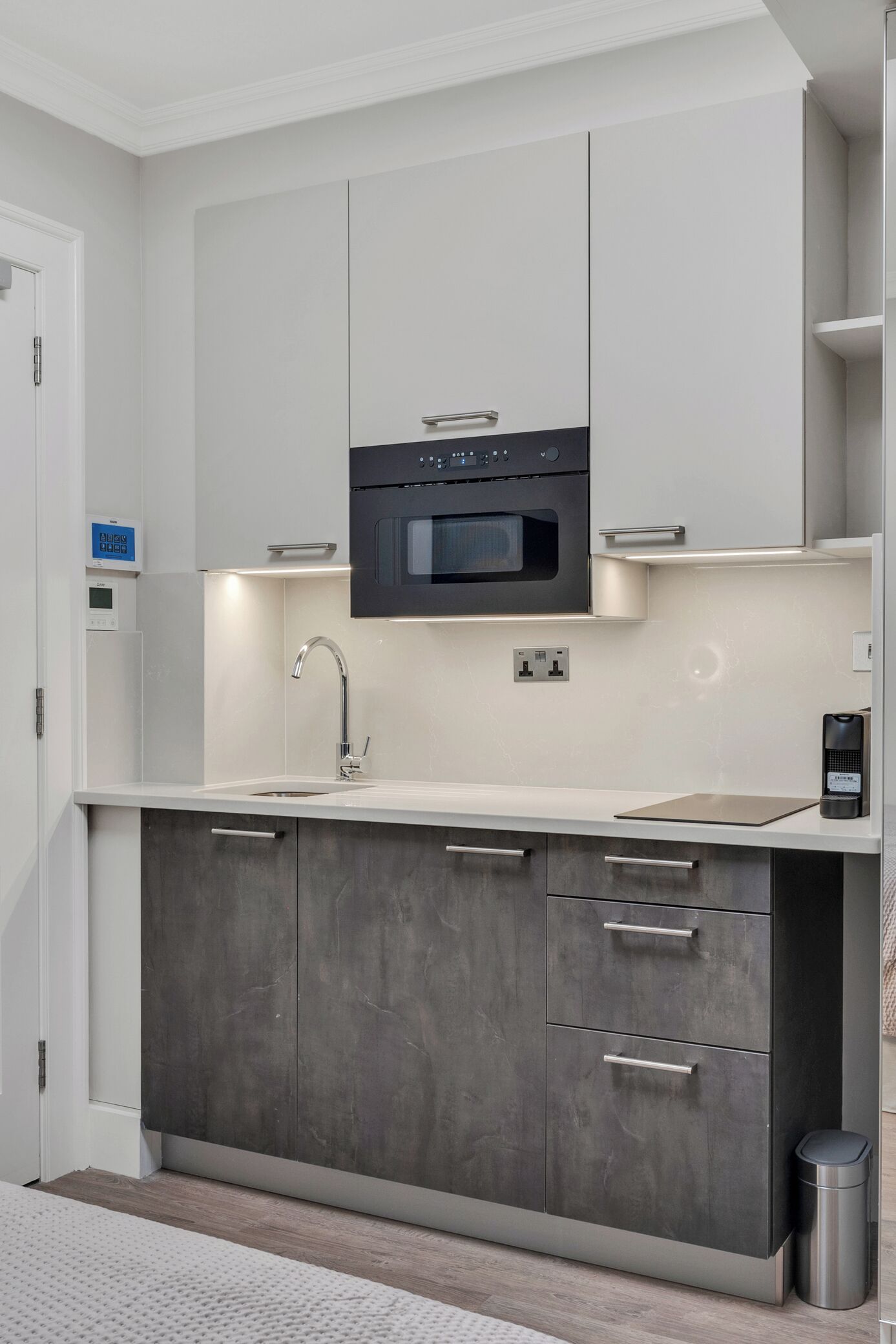 A modern kitchen with a built-in oven, a stainless steel sink, and a dark grey cabinet with drawers.