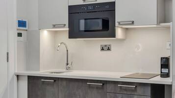 A modern kitchen with a built-in oven, a stainless steel sink, and a dark grey cabinet with drawers.