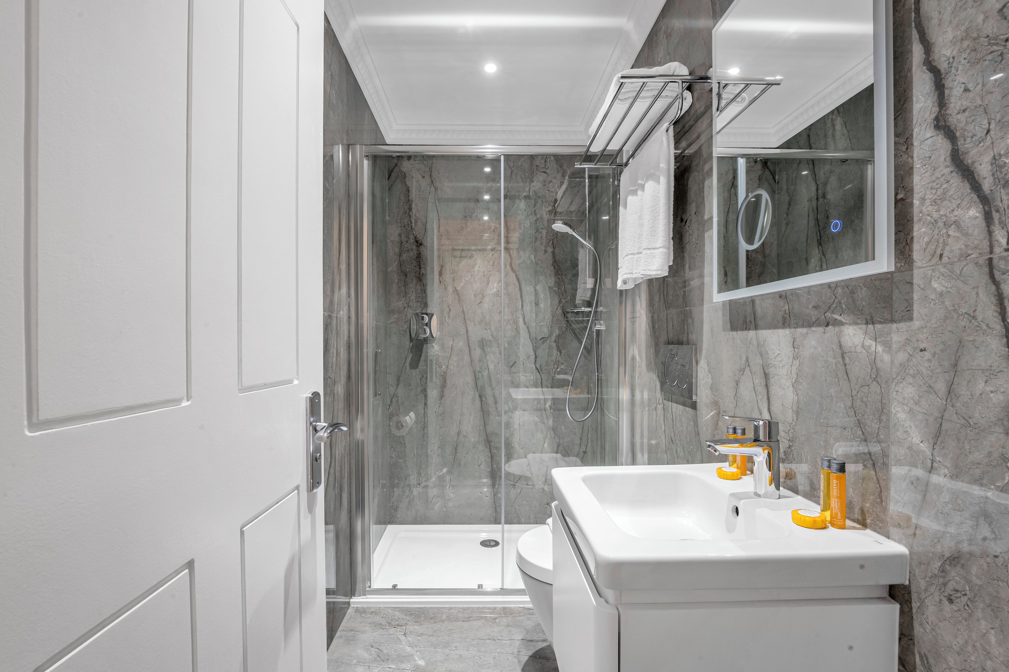 A modern bathroom with a glass-enclosed shower, a white sink, and a marble wall.