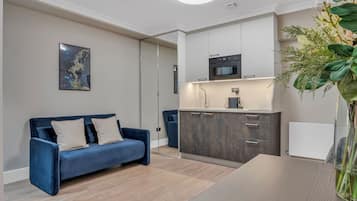 A modern living room with a blue sofa, a dining table, and a kitchen area with cabinets and appliances.