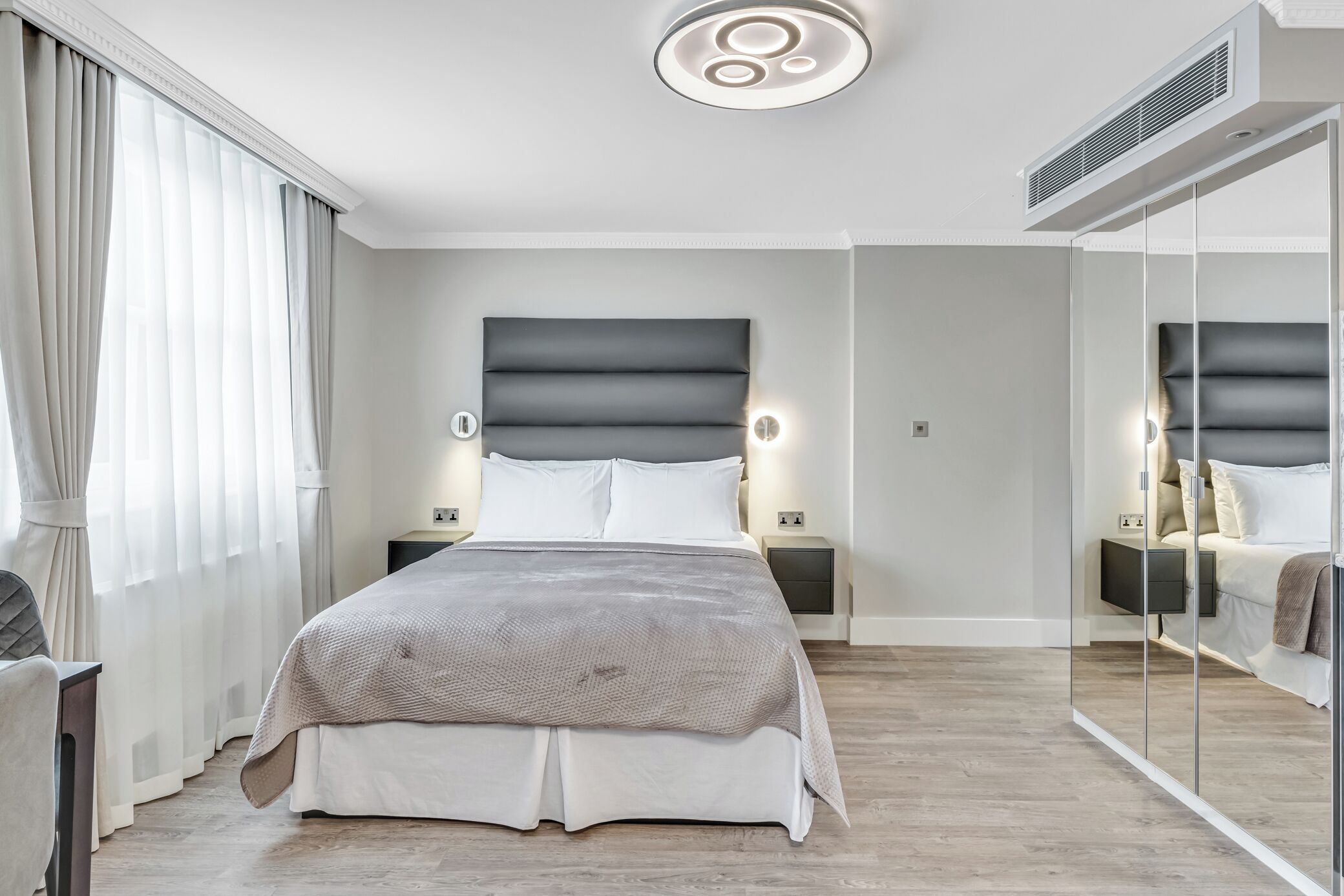 A modern bedroom with a large bed, bedside tables, a mirror, and a ceiling light fixture.