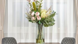 Un tavolo da pranzo con un vaso di fiori, due poltrone imbottite e una finestra con tende leggere.