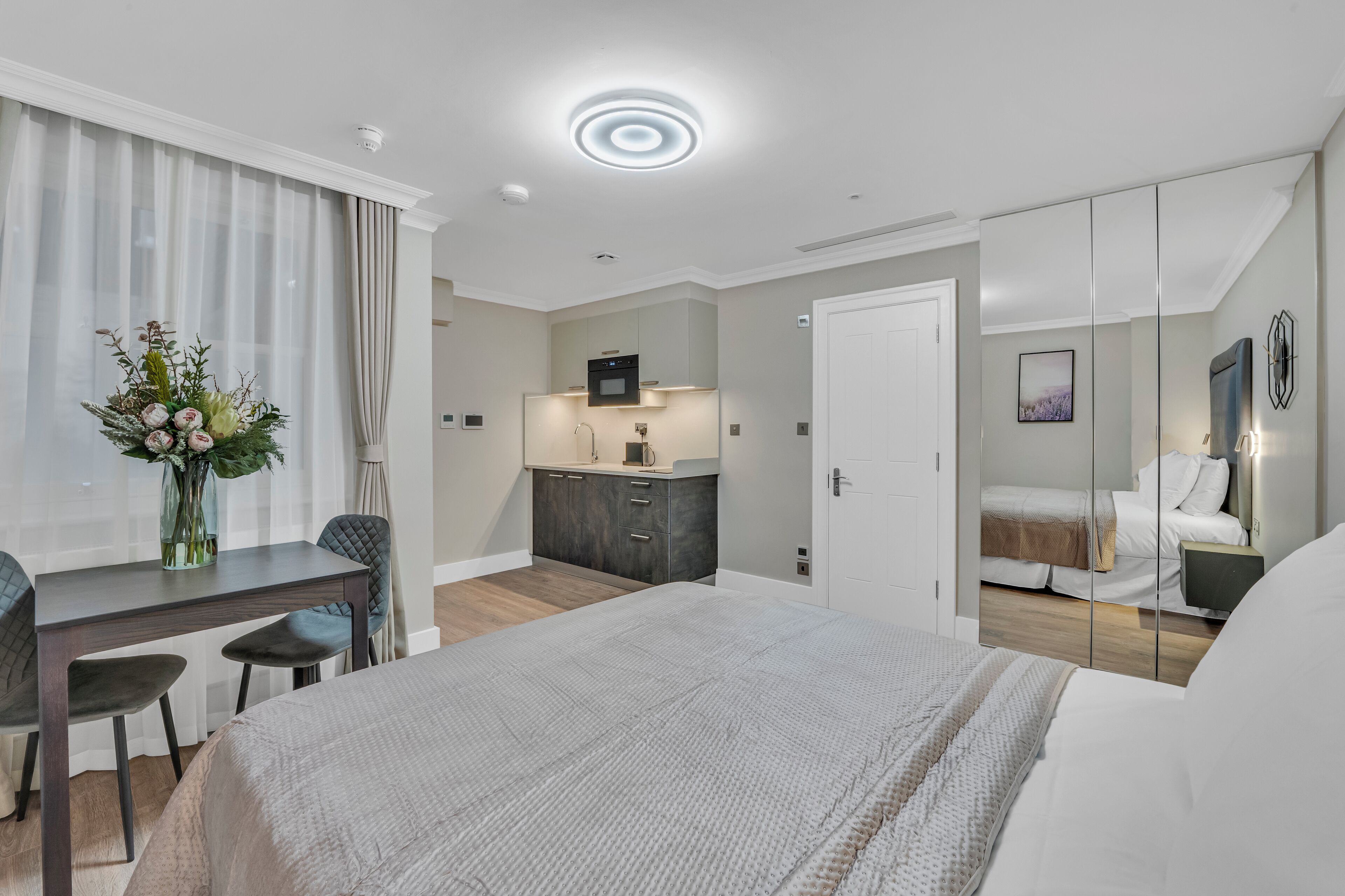 A modern hotel room with a bed, a desk, a small kitchenette, and a bathroom.
