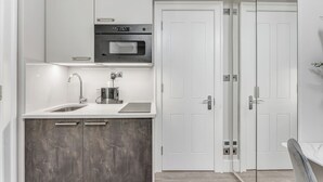 Una cucina moderna con forno integrato, microonde e lavello in acciaio inossidabile. Sono presenti due porte che conducono ad altre stanze.