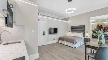 A modern hotel room with a kitchen area, a large bed, a bedside table, and a mirror.