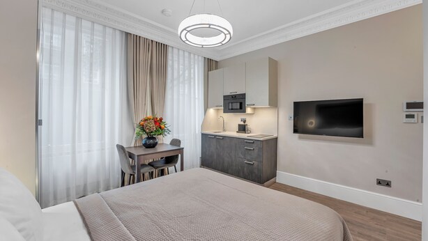 Una camera d'albergo con un letto, una scrivania con una sedia, un angolo cottura e una TV a parete.