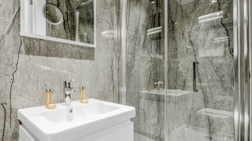 Ein modernes Badezimmer mit einem weißen Waschbecken, zwei Shampooflaschen, einem Spiegel und einer Duschkabine.