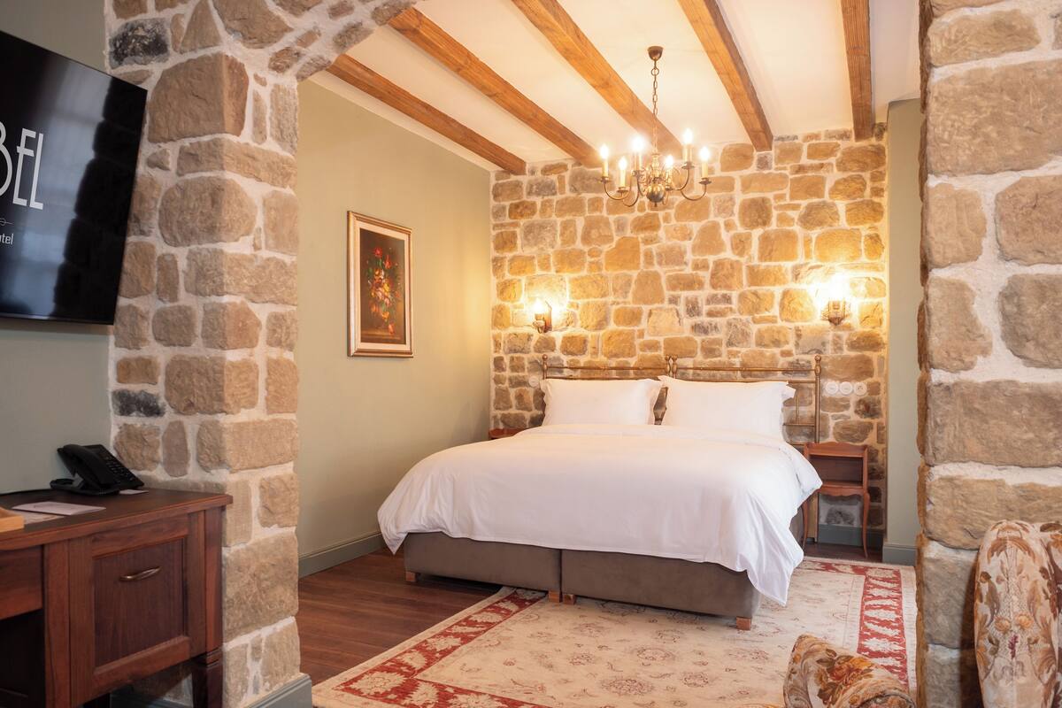 Ein Schlafzimmer mit Steinsandsteinwand, einem Bett, einem Nachttisch, einem Fernseher, einem Schreibtisch und einem Stuhl.